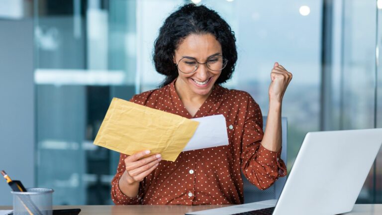 Femme enthousiaste lisant lettre devant ordinateur.