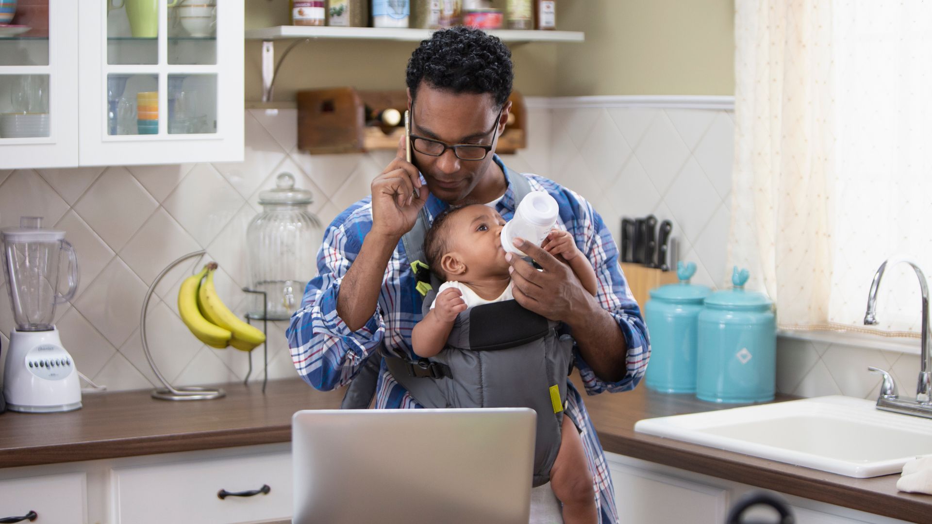 Père multitâche nourrissant bébé en porte-bébé et téléphonant.