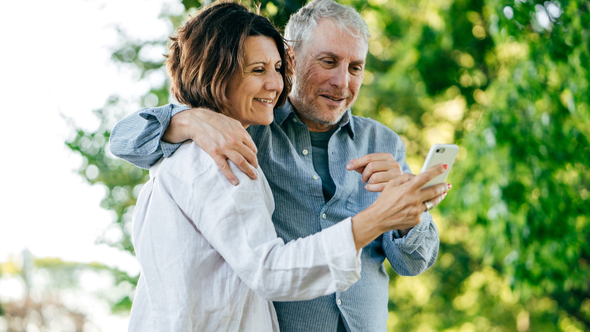 Couple senior souriant avec smartphone en extérieur.