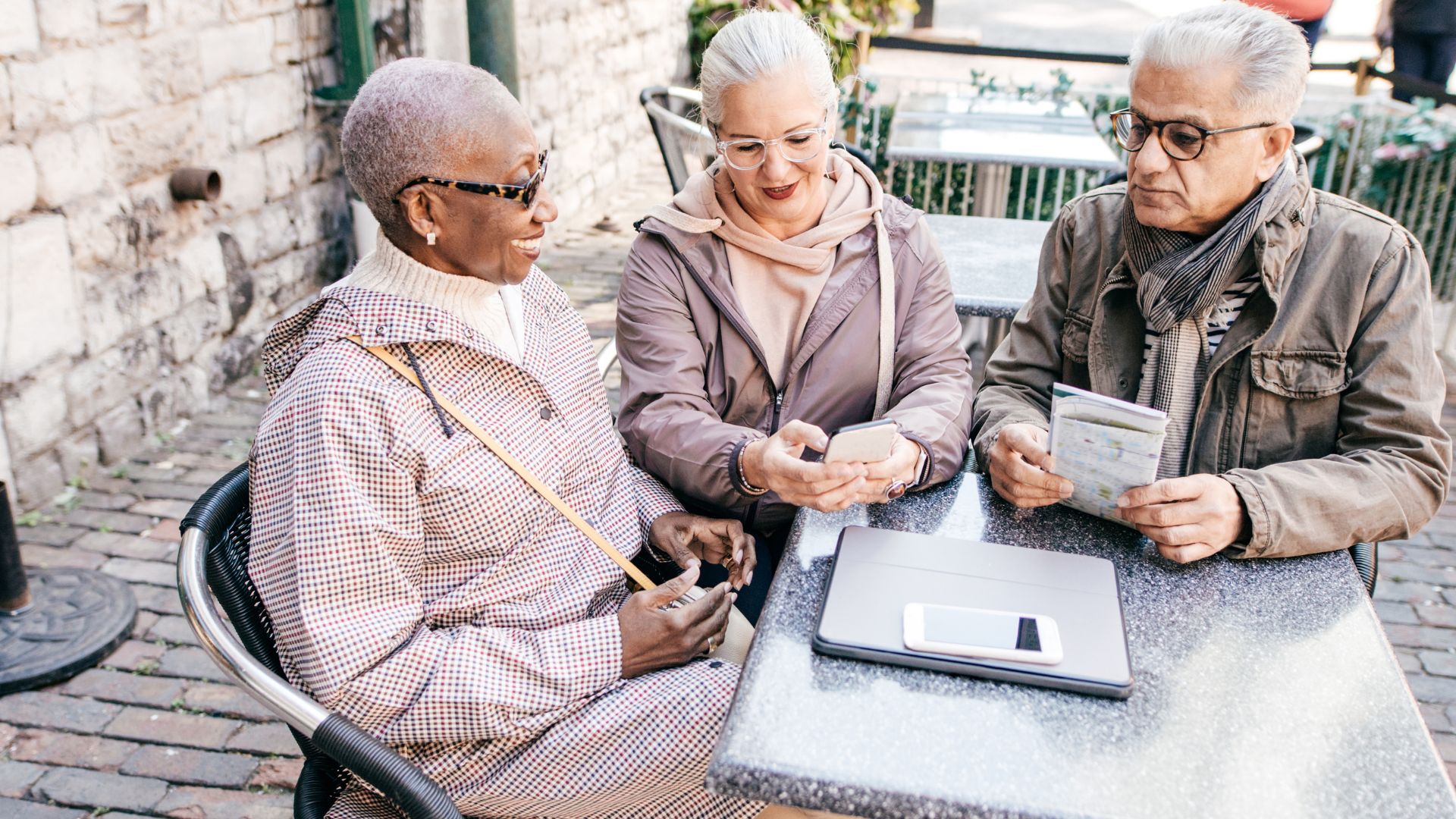 Trois seniors utilisant smartphone et tablette en extérieur.
