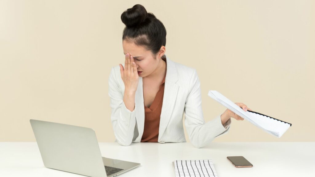 Femme stressée avec ordinateur et documents au bureau.