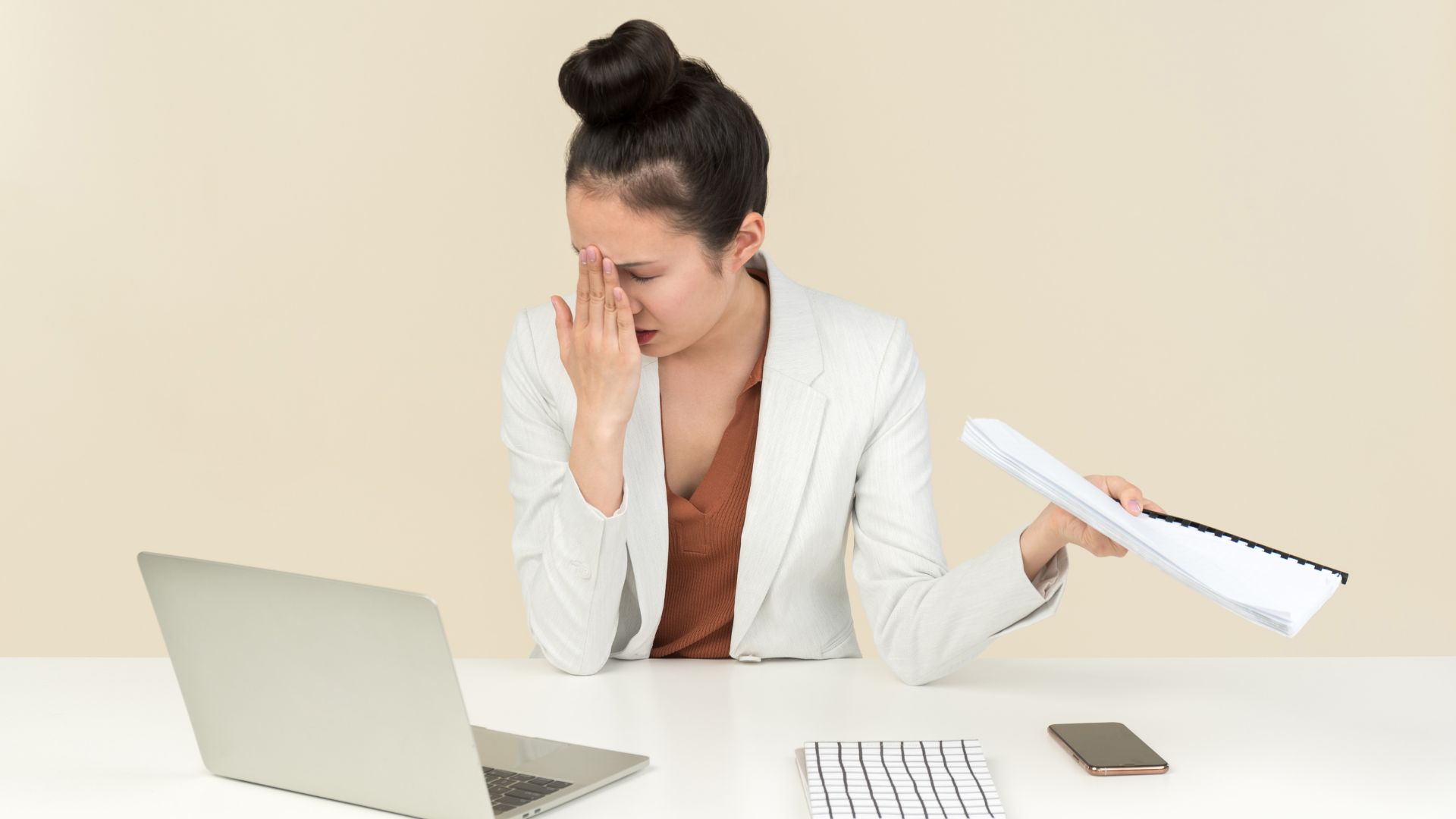 Femme stressée avec ordinateur et documents au bureau.