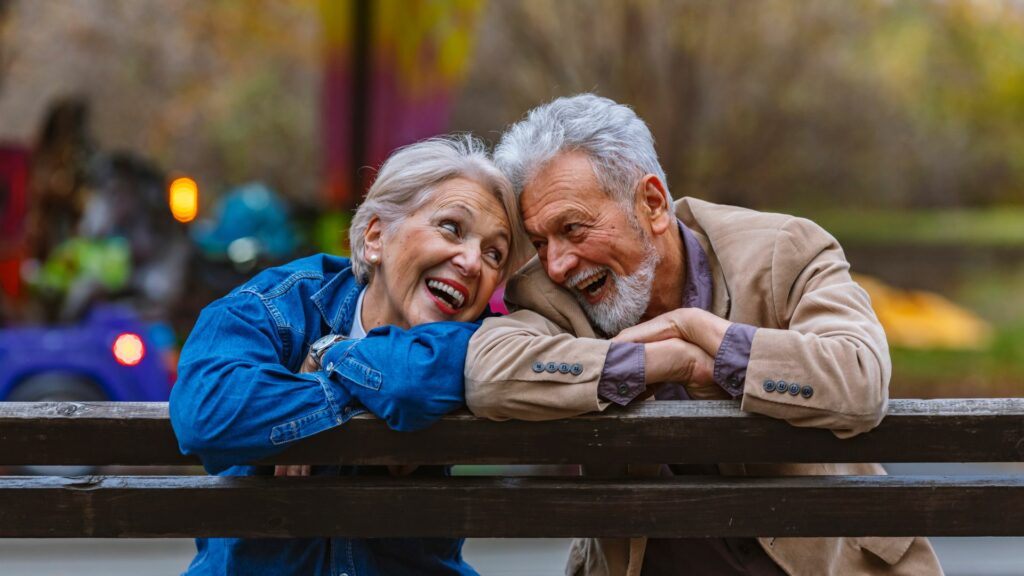 Couple âgé souriant sur un banc en automne.