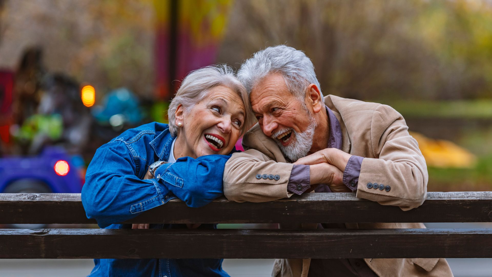Couple âgé souriant sur un banc en automne.