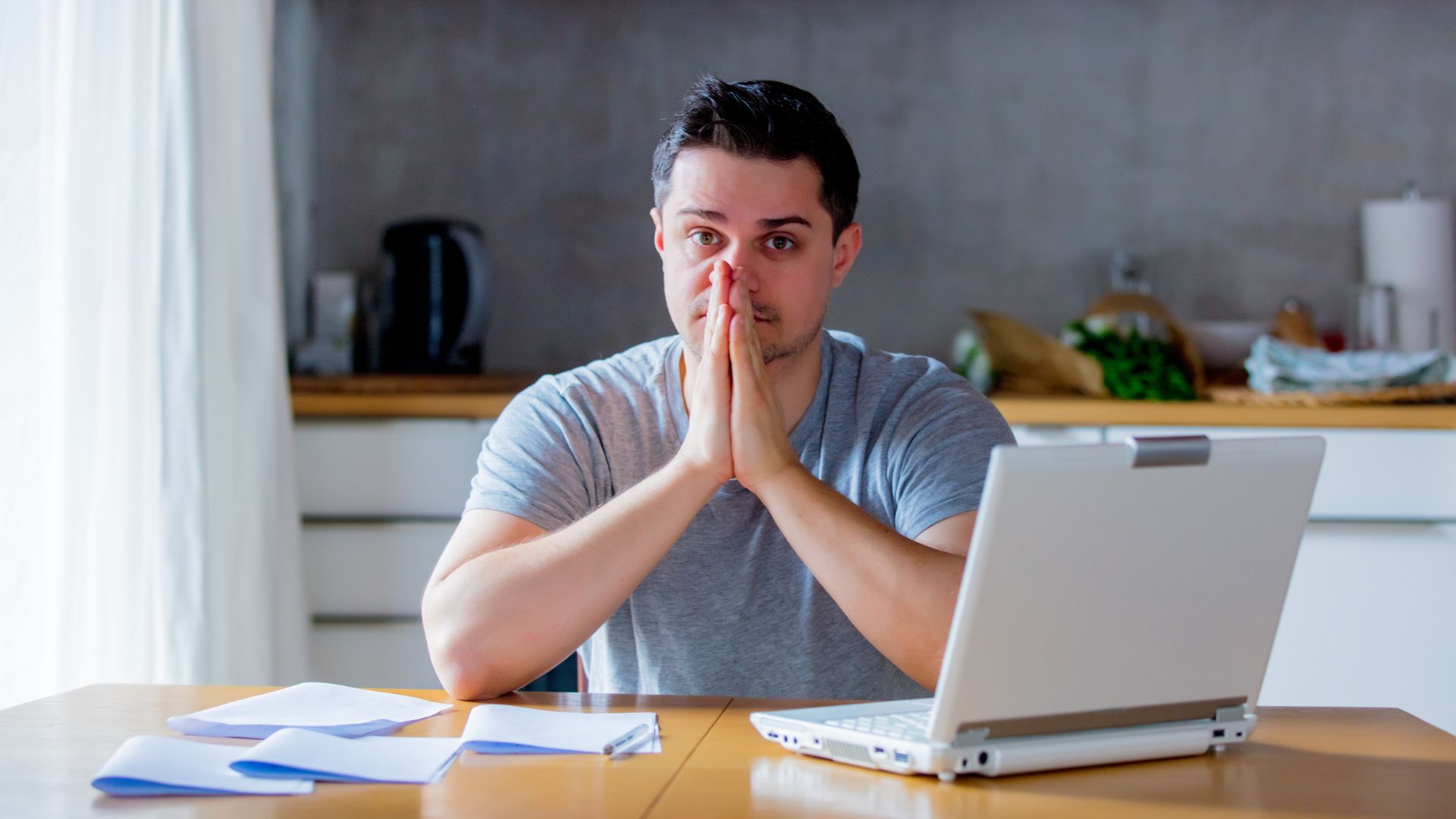 Homme inquiet devant ordinateur, papier, bureau maison.