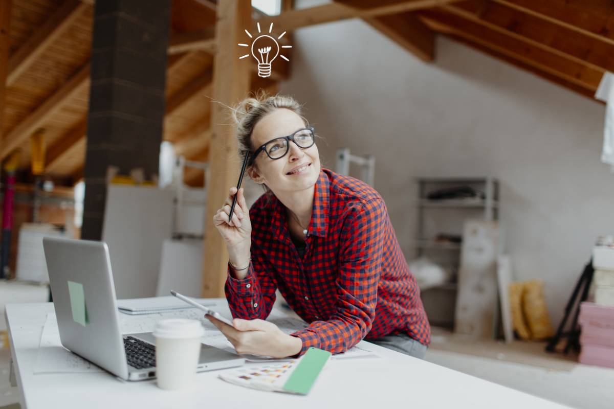 Femme réfléchissant avec ordinateur dans un bureau mansardé.