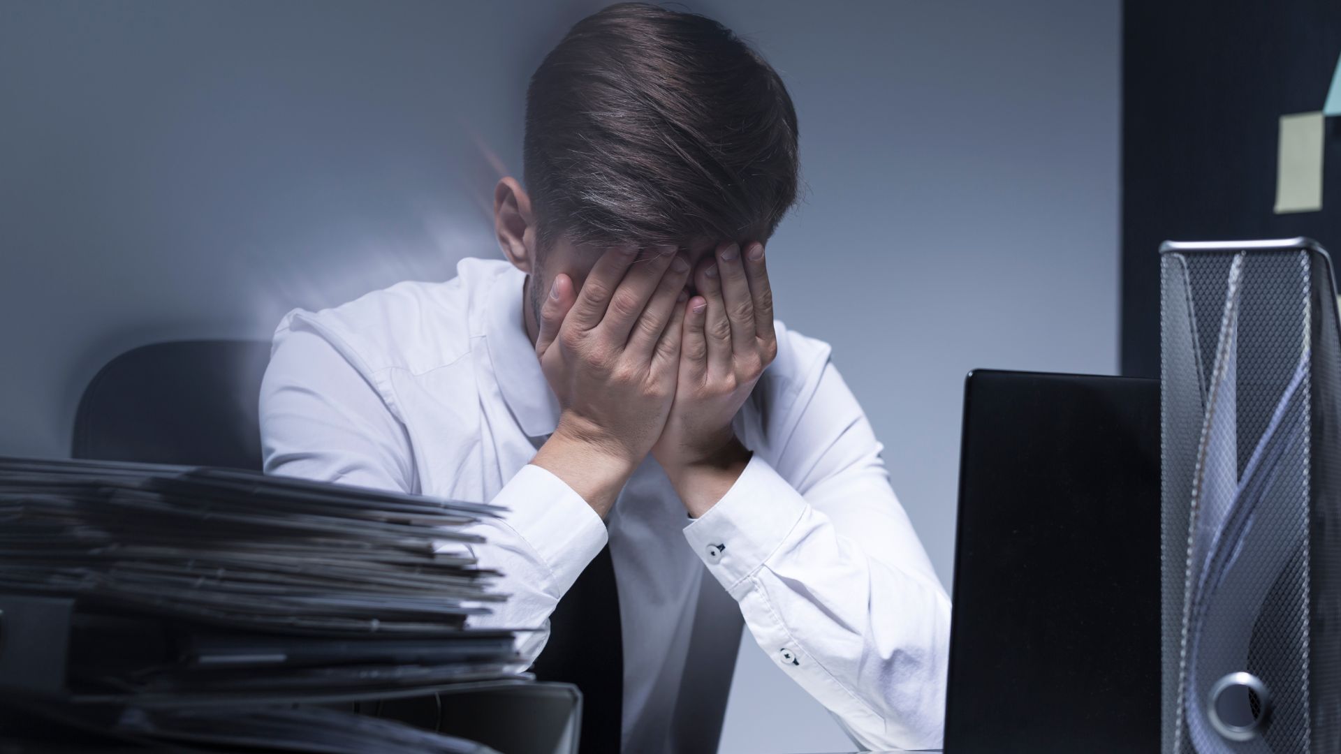 Homme stressé au bureau se couvrant le visage.