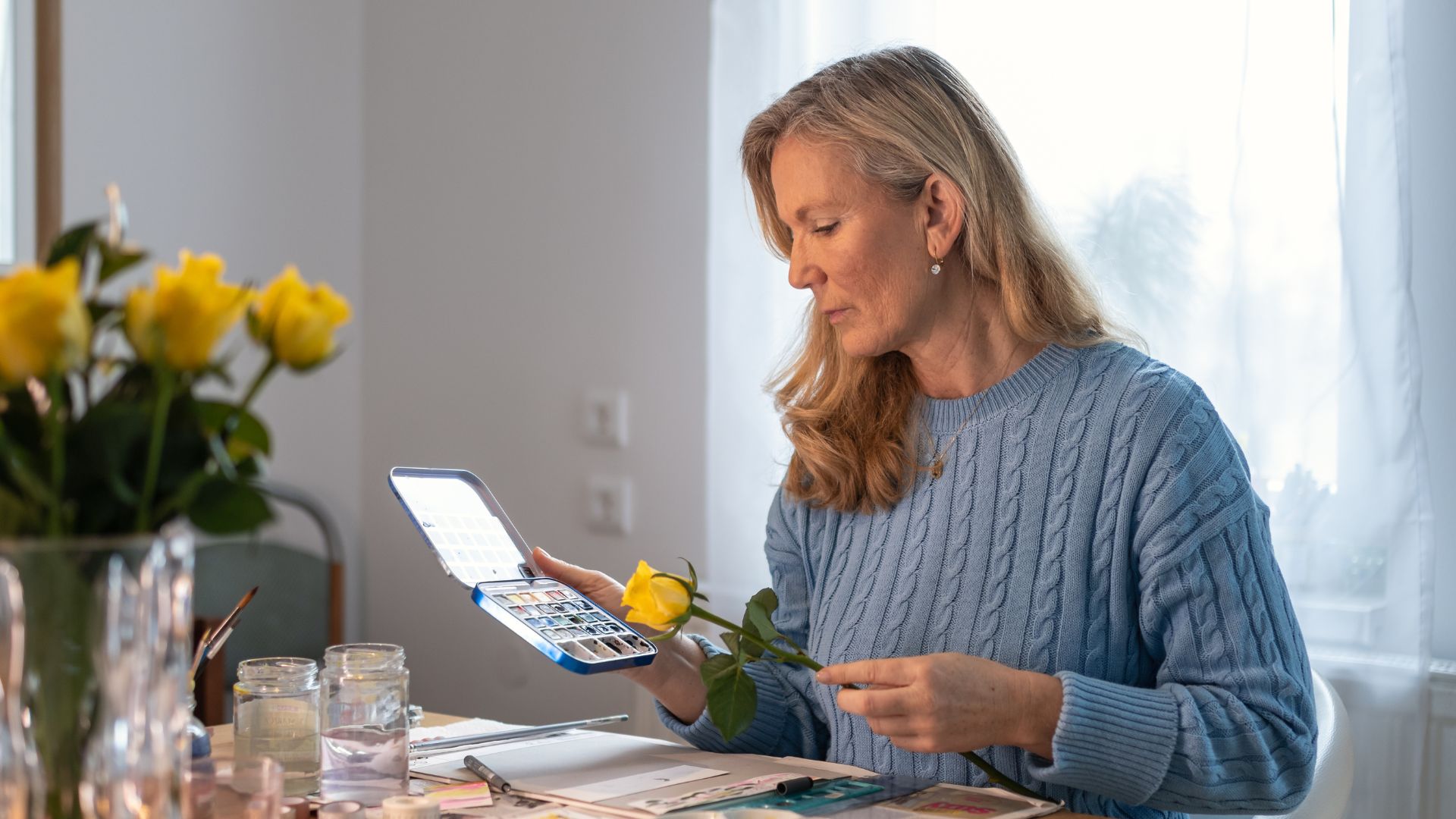 Femme peignant avec palette d'aquarelles et fleurs jaunes.