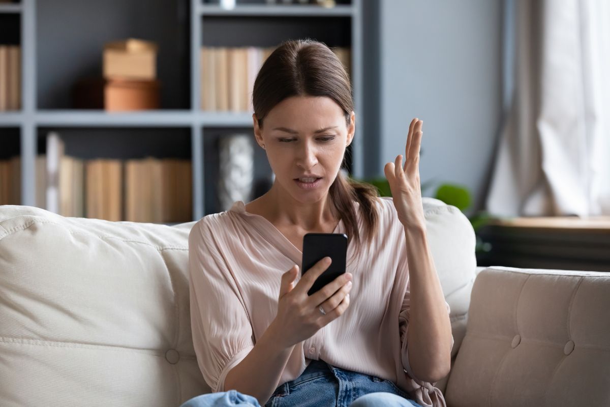 Femme frustrée regardant son smartphone sur un canapé.